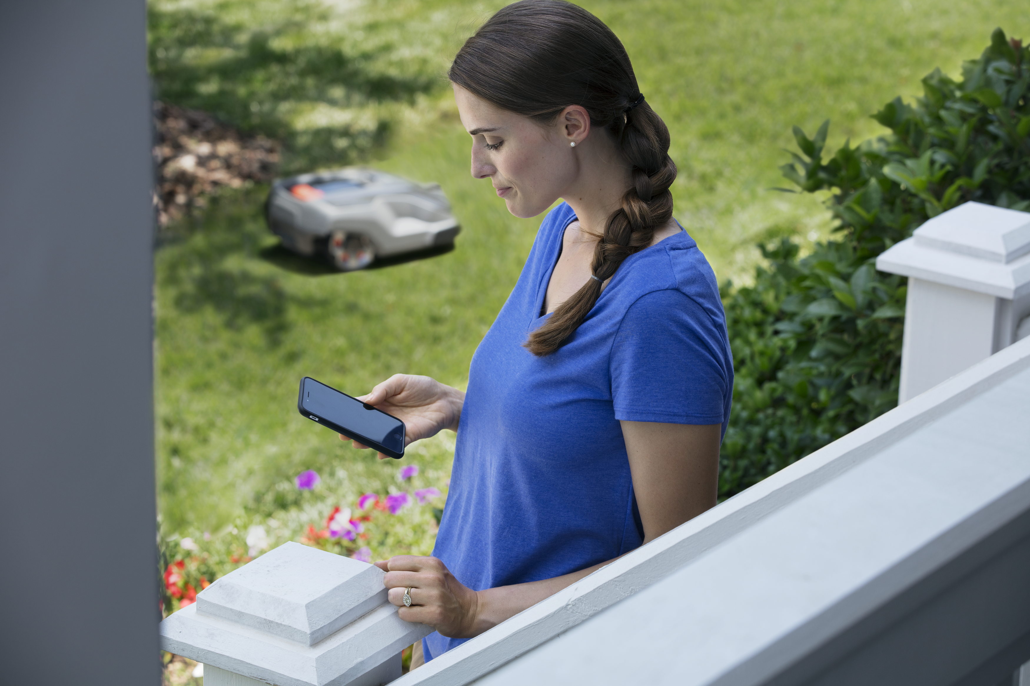 Жінка зі смартфоном і косарка Automower на подвір’ї