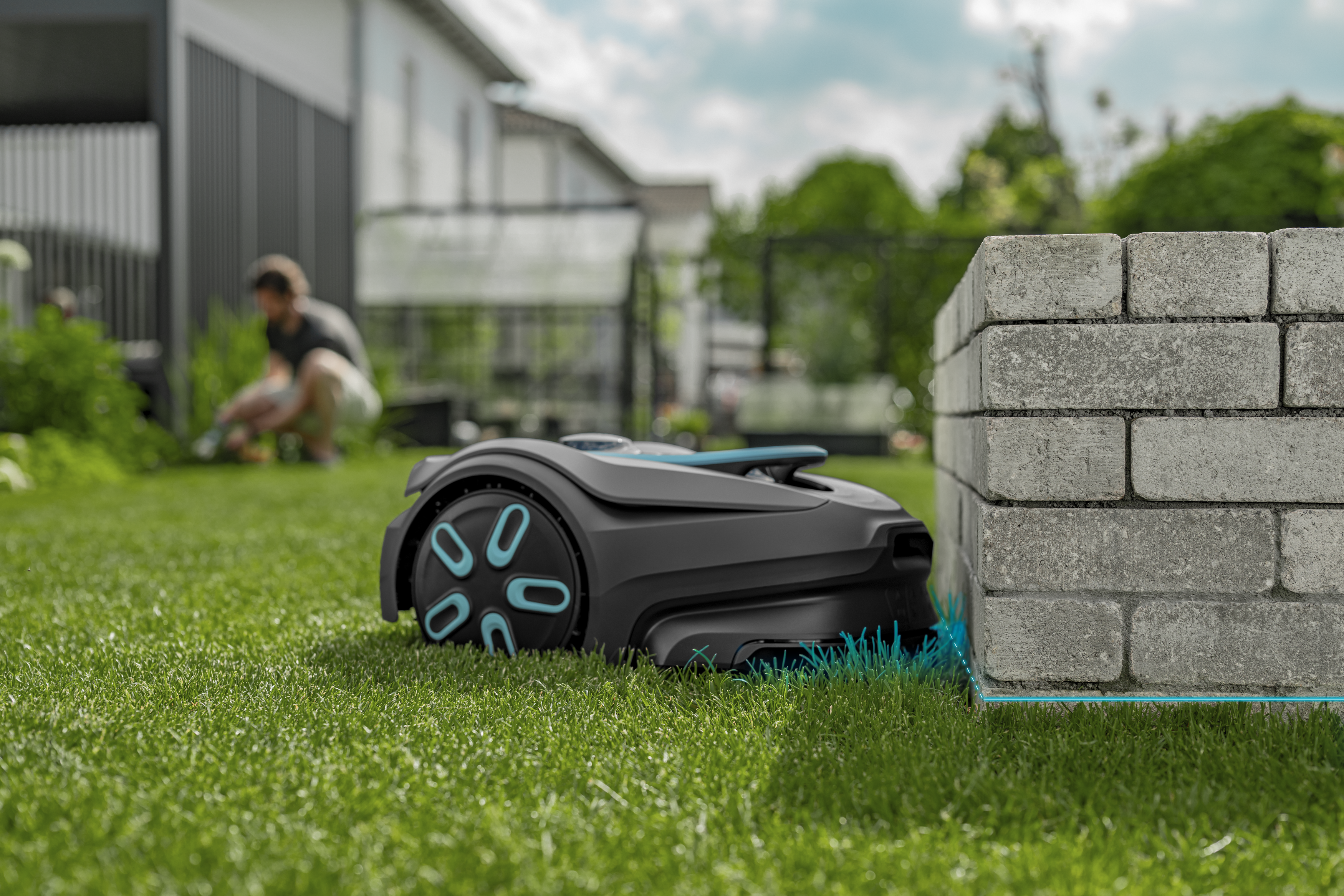 Robotic lawn mower moving along a lawn edge beside a brick wall in a residential garden.