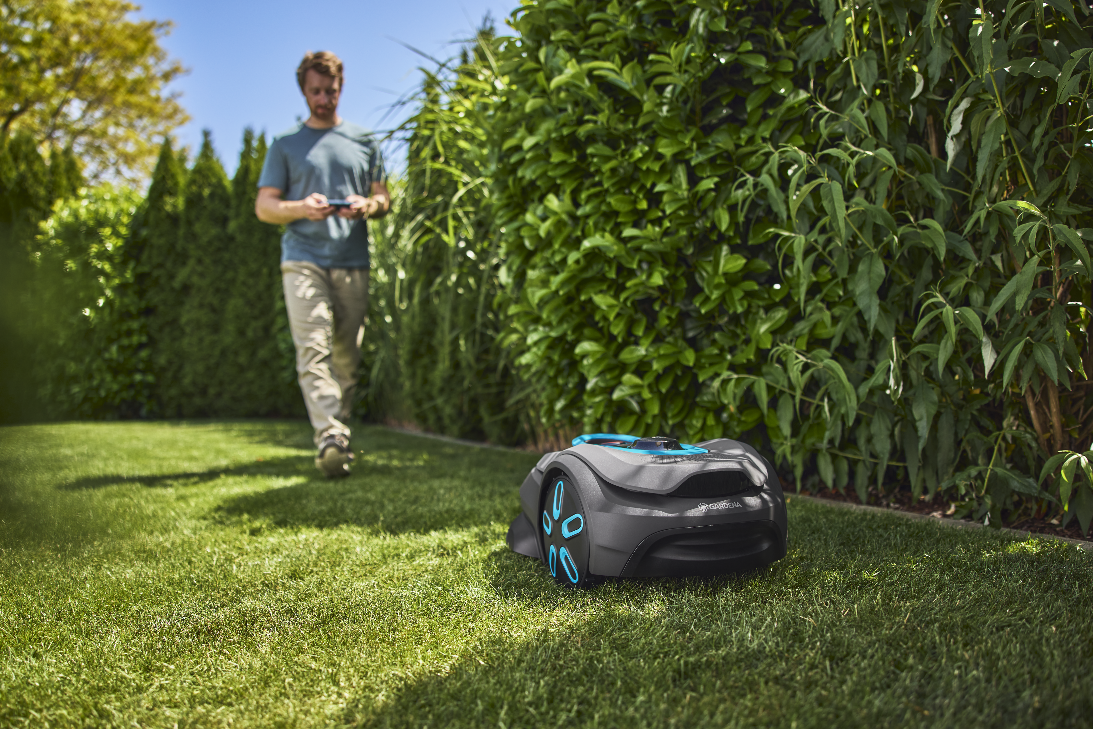 A robotic lawn mower operating on a grassy area with a person standing nearby.