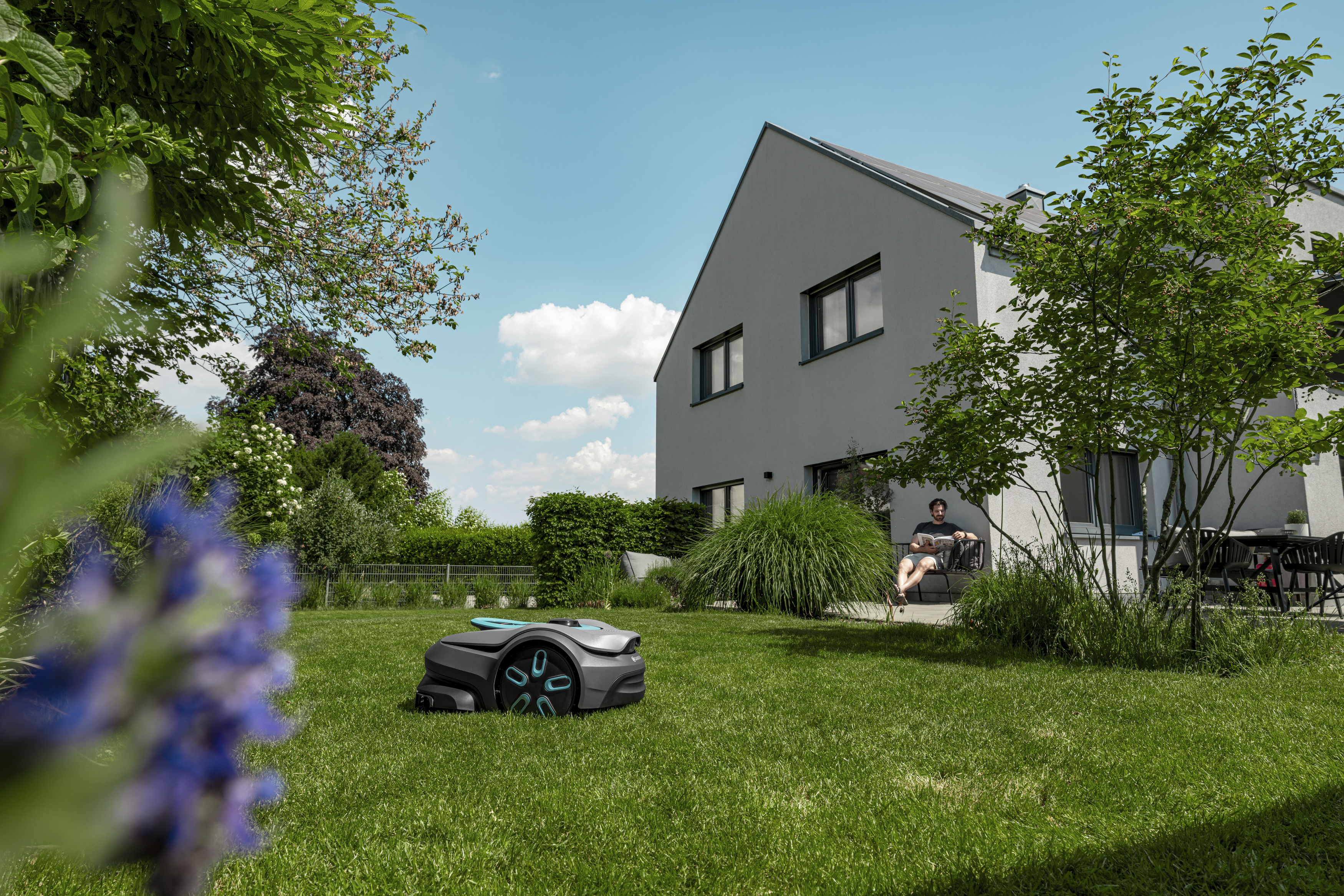 Robotic lawn mower operating on a residential lawn beside a modern house and garden.